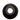 A single black circular rubber or plastic component with a hollow center, photographed on a plain white surface with a bright overhead light reflection above it.
