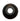 A single black circular rubber or plastic component with a hollow center, photographed on a plain white surface with a bright overhead light reflection above it.